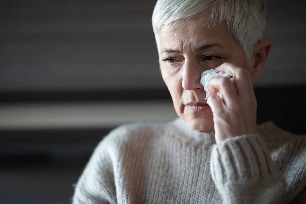 A mature woman wiping tears from her face.