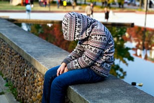 Depressed Child sitting sadly on a bench, head bowed.