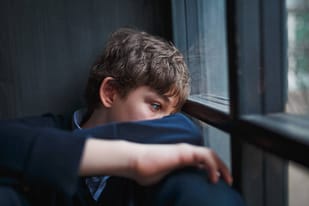 Boy you lacks self-esteem leaning against the window frame, head down.