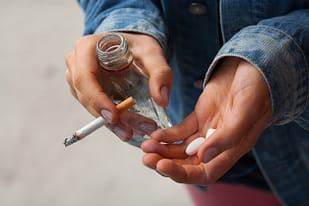 Teen holding drugs, vodka and a lit cigarette, showing a drug addict.