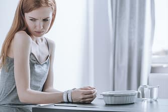 Very skinny young woman with her wrists tied together with a measuring tape, suffering from an eating disorder.