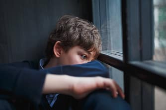 Boy you lacks self-esteem leaning against the window frame, head down.