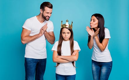 Parents fawning over child wearing a crown, arms crossed.